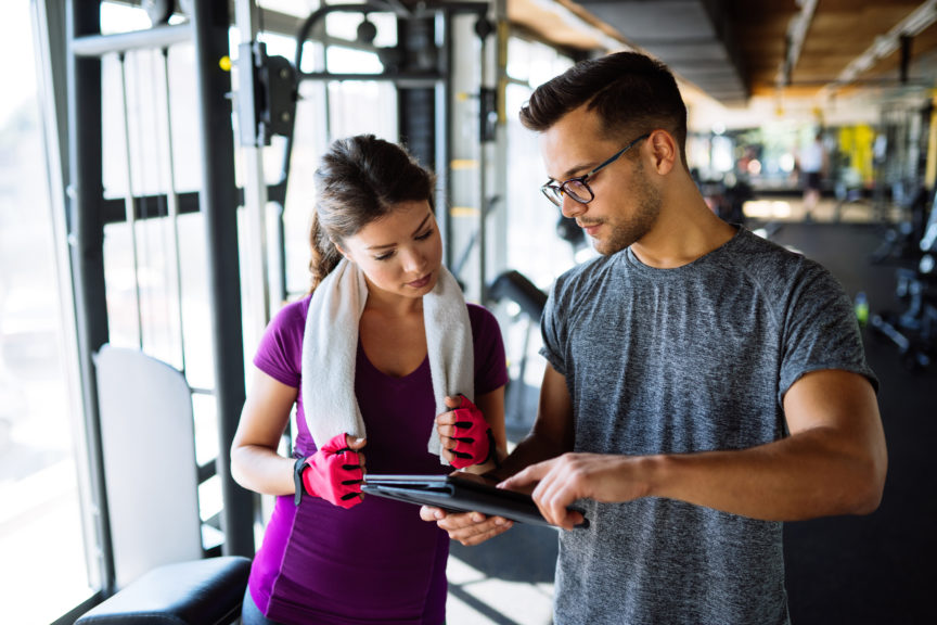 Woman and personal trainer making exercise plan in gym